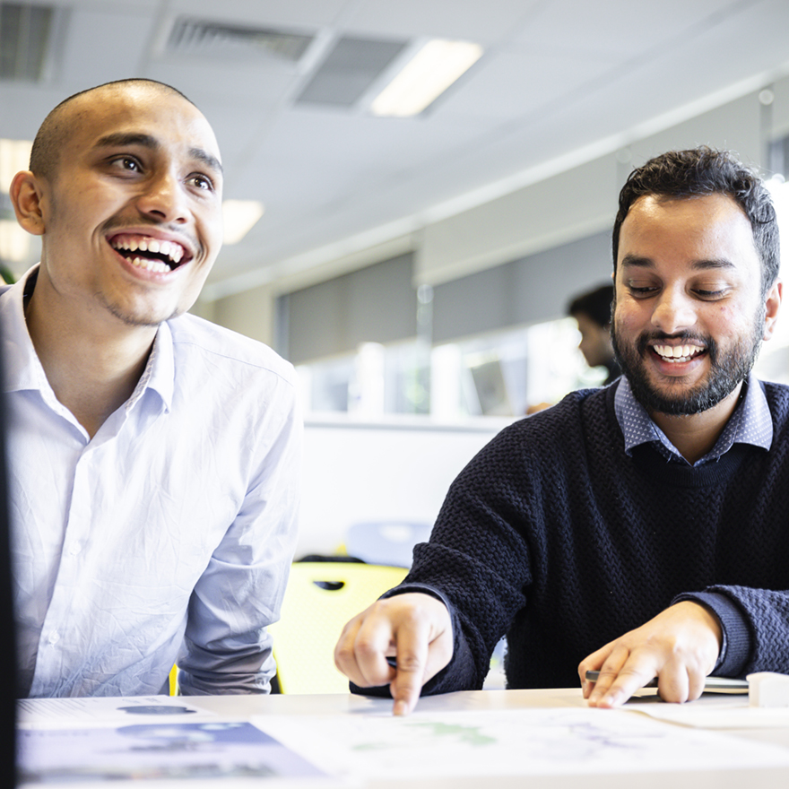 Two students discussing their work at a desk