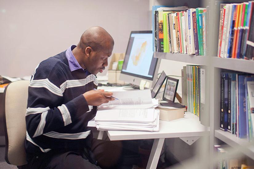 Man sitting at desk with books, computer and written notes