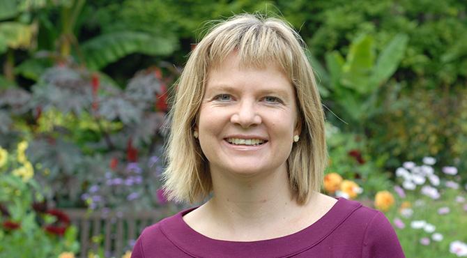 A headshot of Heather smiling with a garden in the background