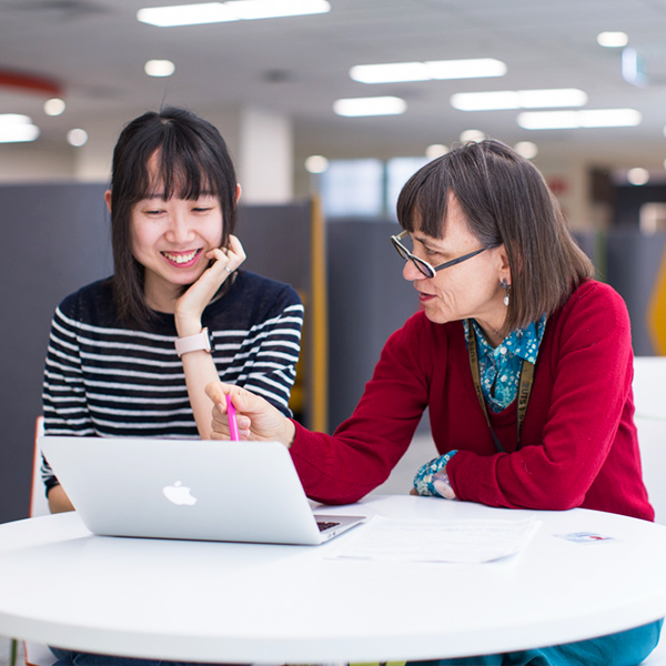 A teacher sitting with a student, pointing to a laptop