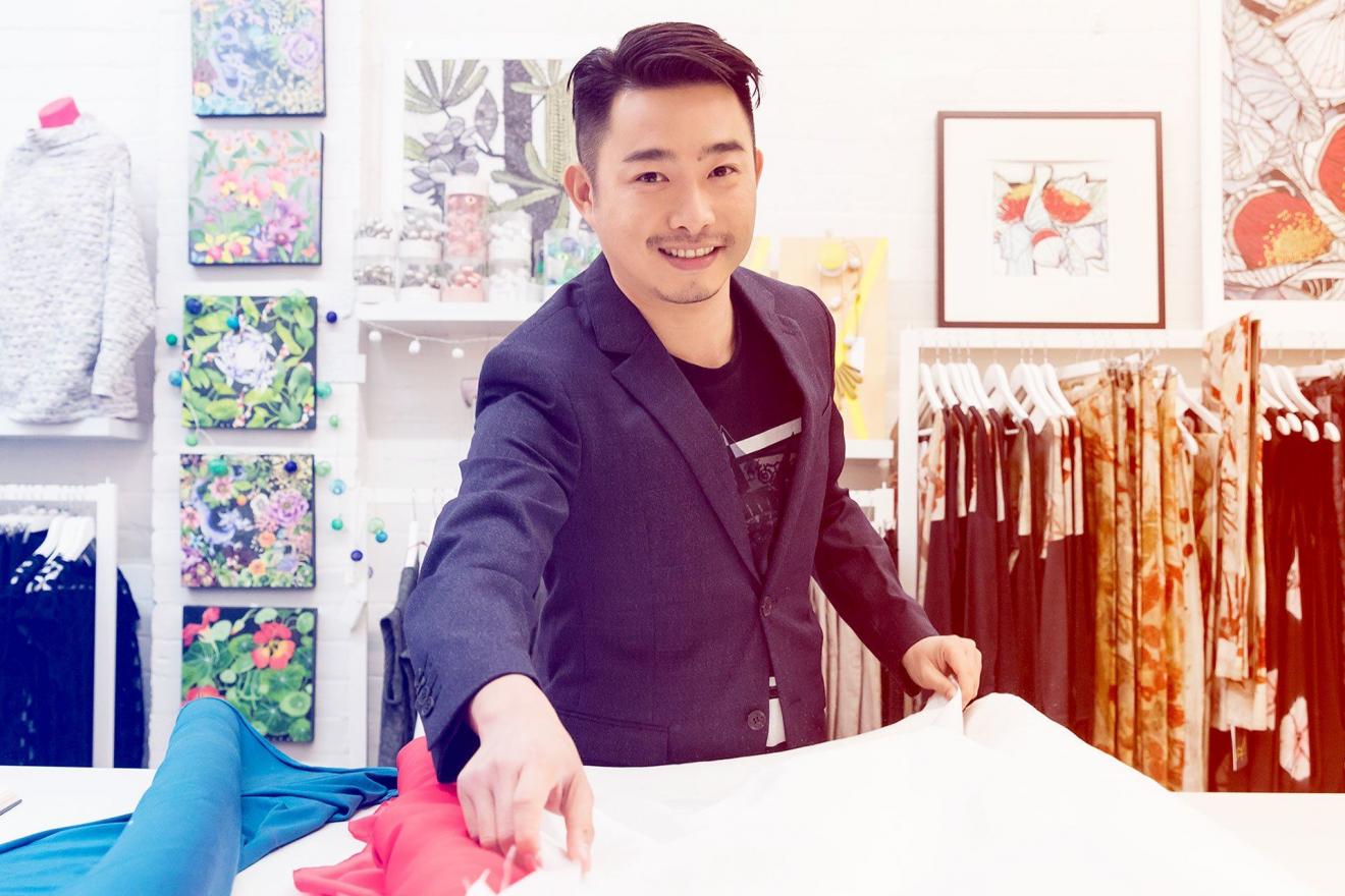 Man at work bench with fabric and clothing rack behind him