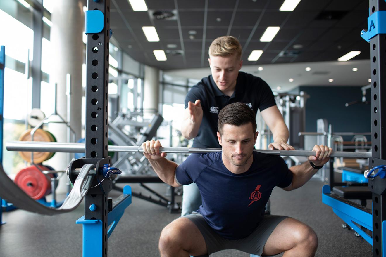 Man being instructed lifting wights in a gym setting