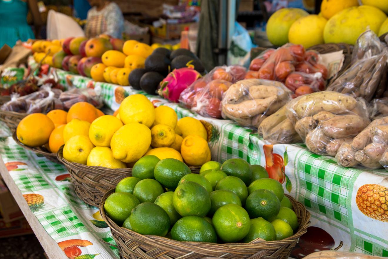 A food market in the Pacific, with bowls of lemons and limes in the foreground and other vegetables behind them