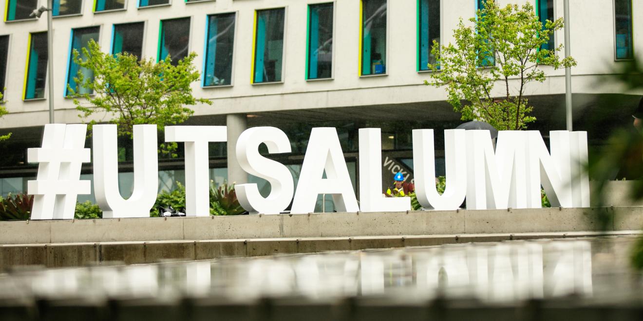 sign #utsalumni with trees and a building in the background