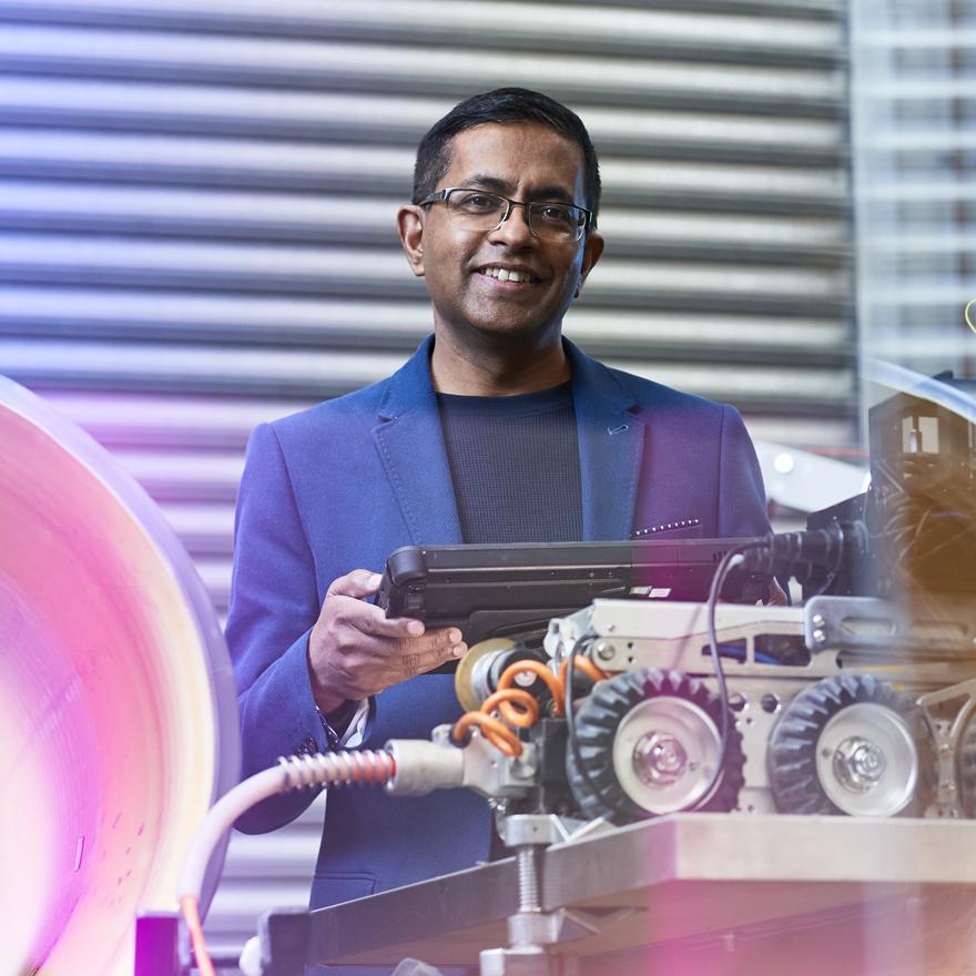 man  in suit with electronic device in hand controlling the robot in the foreground