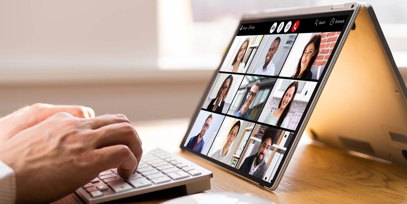 Person typing at keyboard while watching a video conference call on a tablet