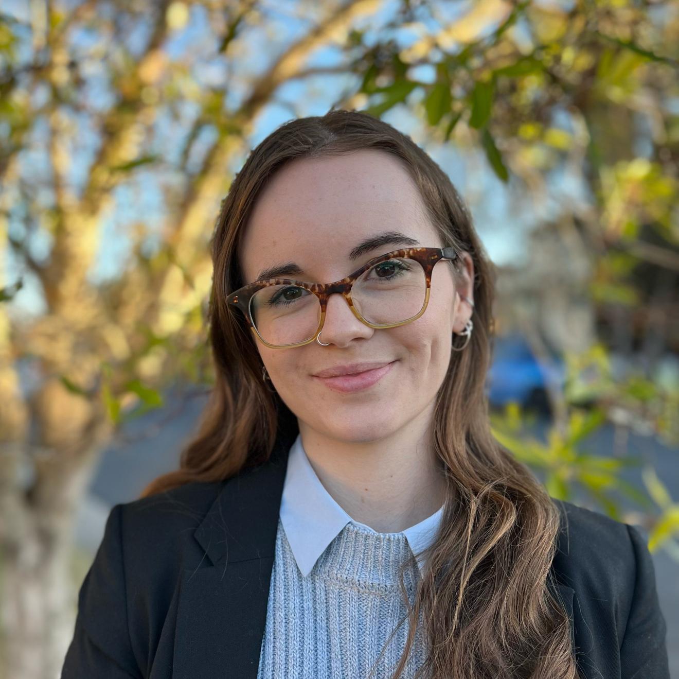 Harriet smiles at the camera while wearing glasses and a black jacket