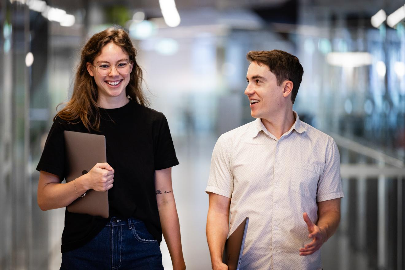 A PhD student and her supervisor walking down a hall with laptops