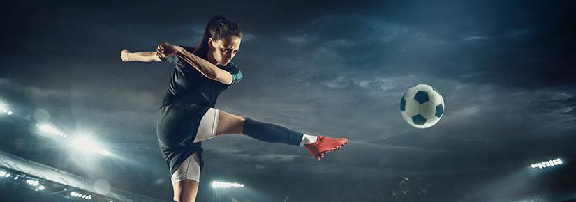 Football player leaping to kick ball in stadium