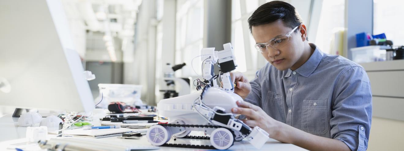 A student works on a small robotic car in a light, bright laboratory