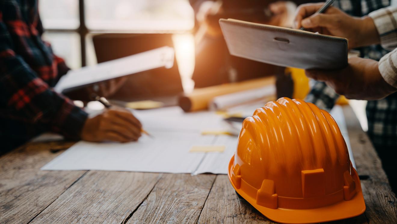 Professionals working around a table, with a hard hat and papers on the table.