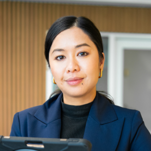 A picture of Danet Chapman, dark hair, gold earrings, wearing a dark navy suit jacket with a black shirt.