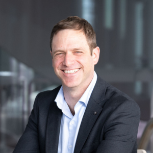 Gilad Francis, light brown hair, smiling, dark suit jacket with a blue collared shirt