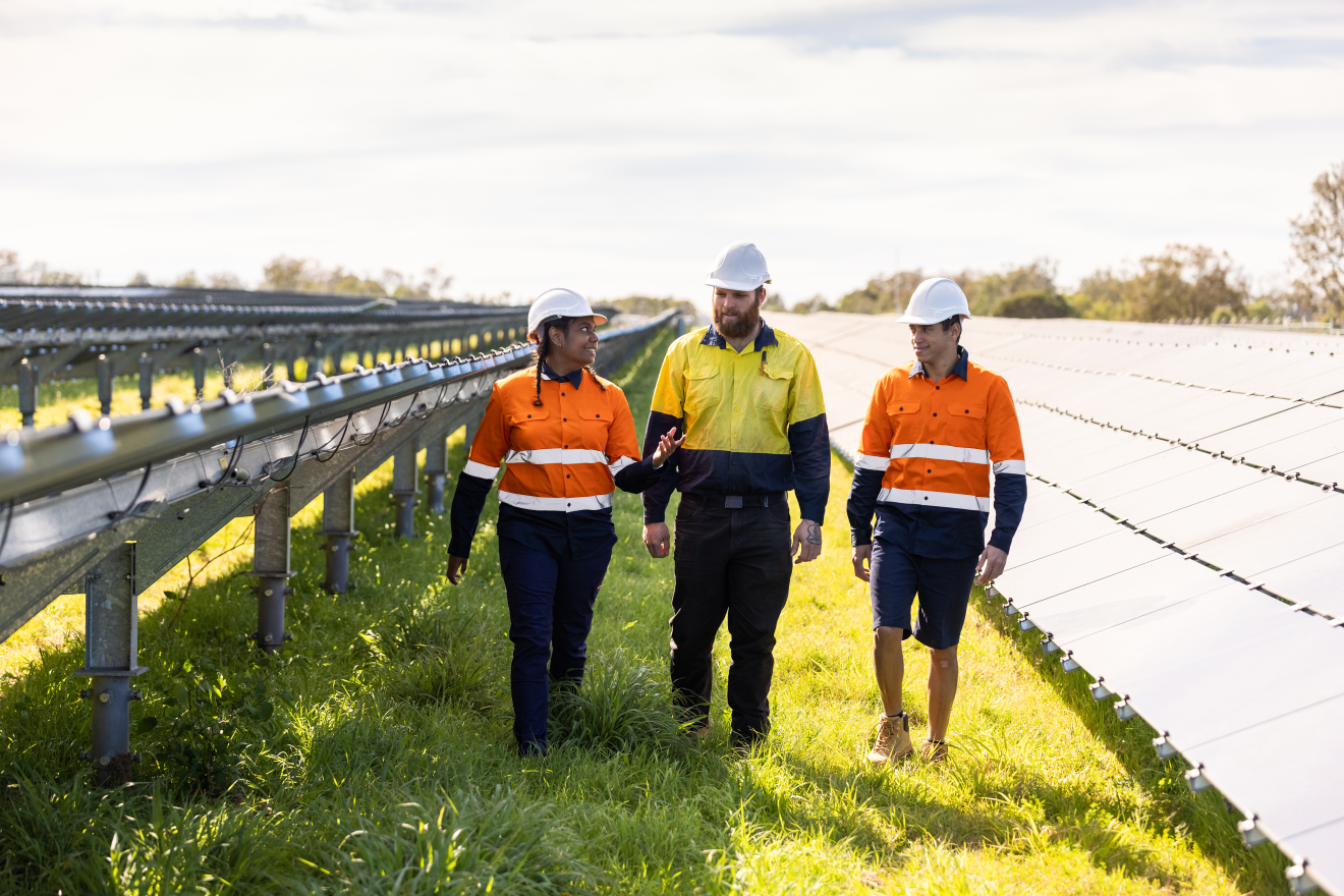 Three renewable energy workers walking through a solar panel field.
