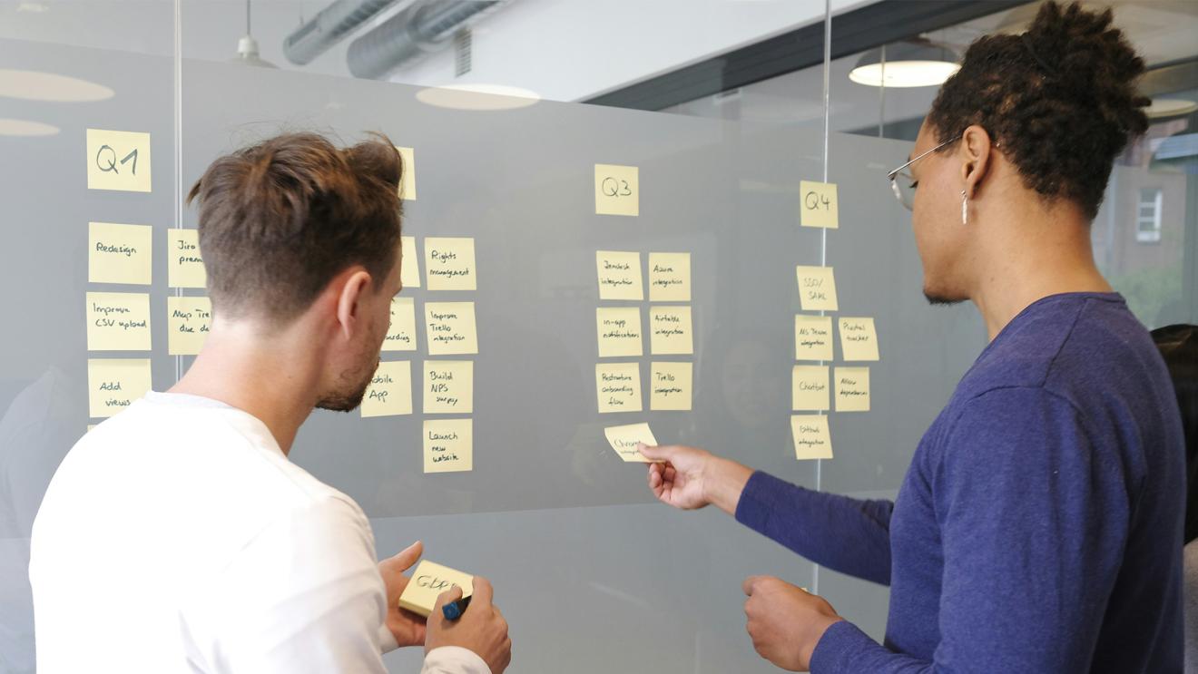 Two students putting project management post-it notes on frosted glass