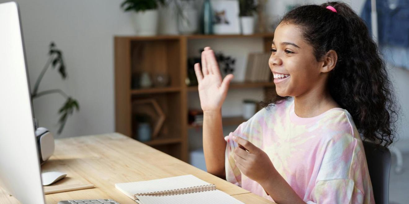 Child in pink shirt raising hand to learn