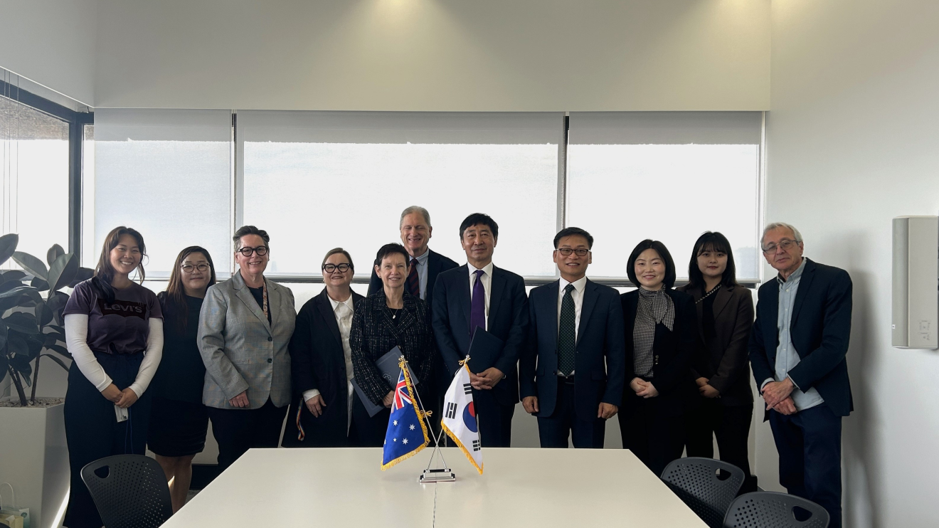 Eleven smiling people standing behind an Australian flag and a South Korean flag.