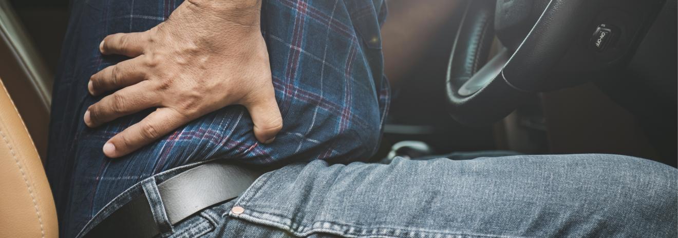 a man holds back in pain, sitting in a stationary car