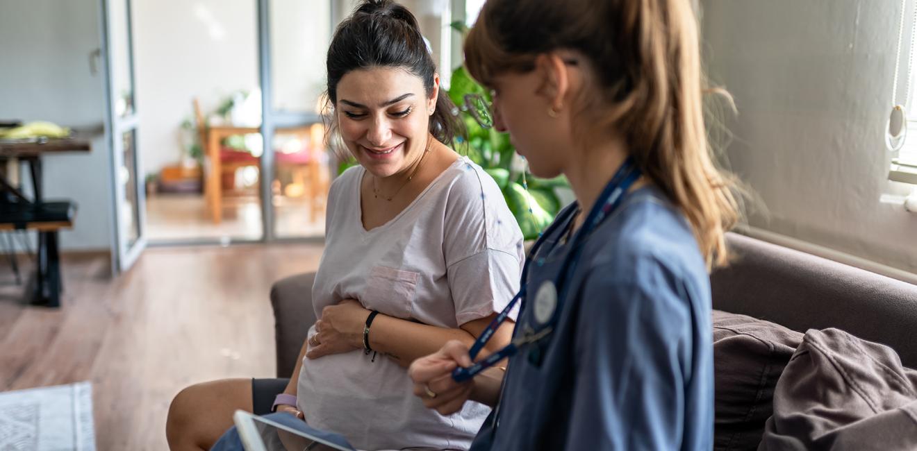 Pregnant woman holding her baby bump looking down with a healthcare professional by her side