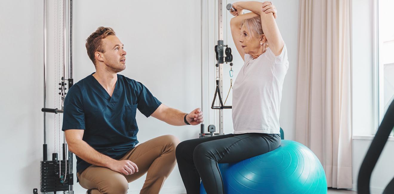 Physio with an elderly lady sitting on an exercise ball doing stretches