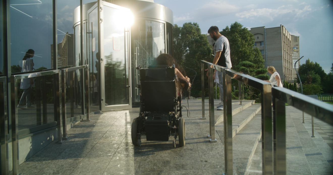 Photo taken of a person in a wheelchair and an able-bodied person entering a building.