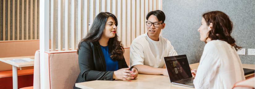 Three student sitting a table and talking. A laptop is on the table in front of one student