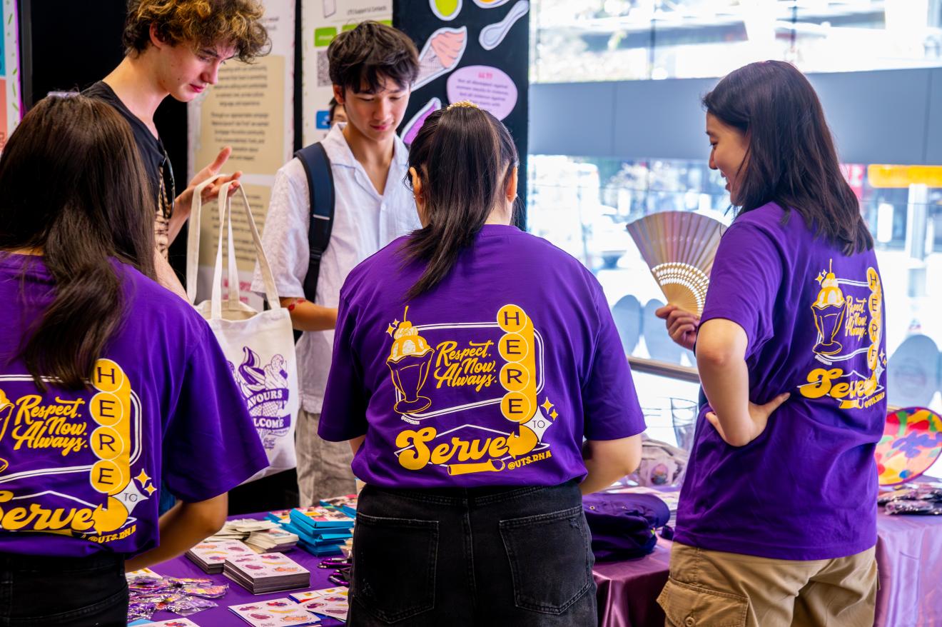 Students at a UTS RNA stall wearing purple 'Respect. Now. Always.' t-shirts, talking with visitors at an O'Day event