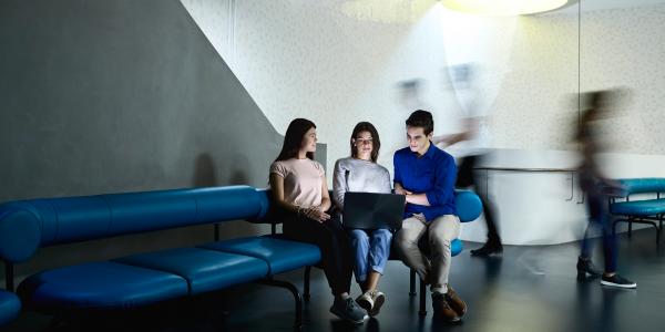 A group of students seated on the lounge gathered around a laptop 