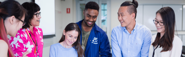 A group of postgrad students in the classroom smiling with a teacher