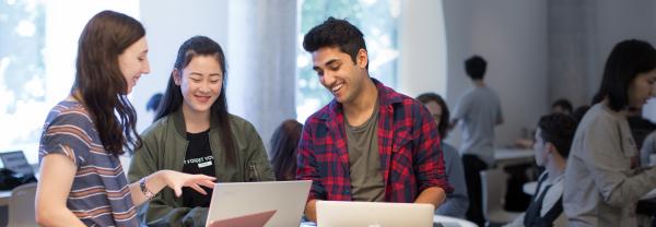 Three smiling students working at a laptop together