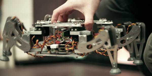 A hand lowers a hexapodic device onto a table from above