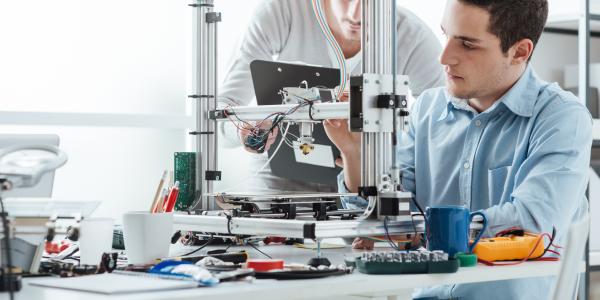 Two men working together at a workstation full of electronic research equipment