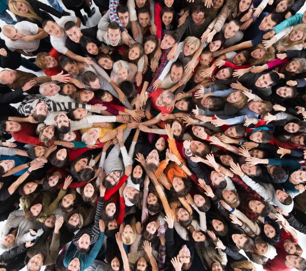 An aerial photograph of a crowd of people, looking up. They are all stretching their arms out into the centre of the group.