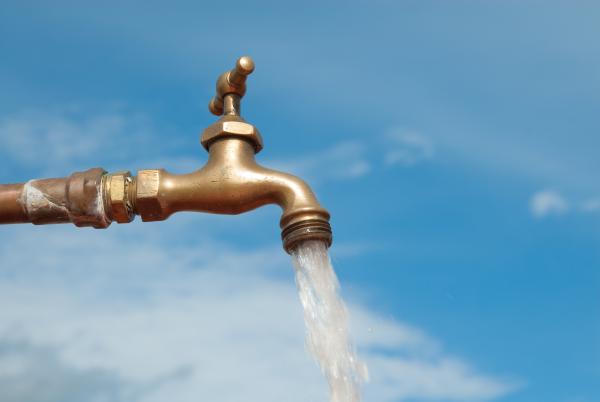 Water runs from a copper-coloured tap. The background is a blue sky.