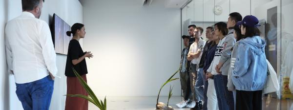 A woman is speaking to a group of young people in the gallery.