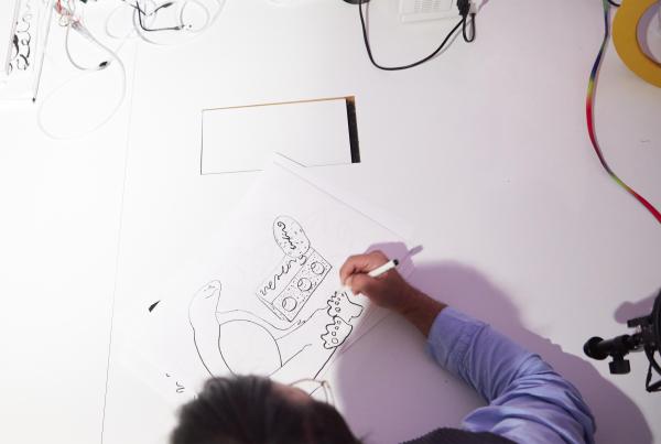 A person is seen from above drawing on a white piece of paper. 