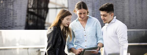 Three students looking at an iPad outside