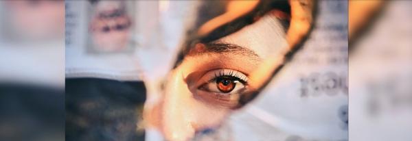 A woman gazes through the tear of a newspaper page in flames