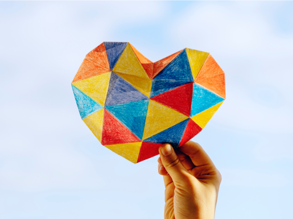 Hand holding up mutli-coloured paper heart.