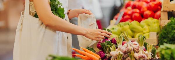 Female hands puts fruits and vegetables in cotton produce bag at food market