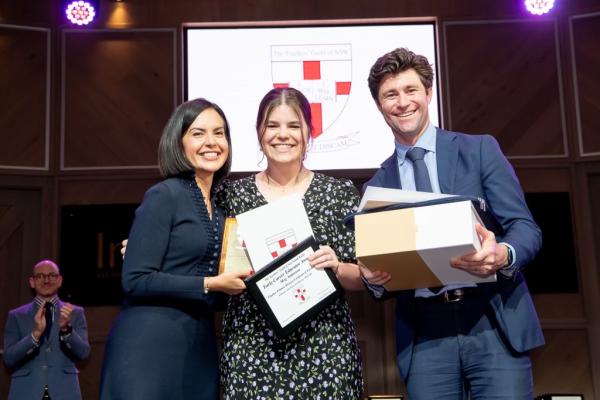 Meg stands on stage with her award with Deputy Premier Prue Car on her right, and a man on her left