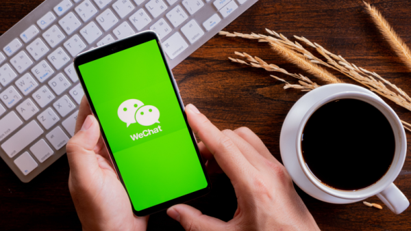 Hands holding mobile with wechat screen, Coffee and keyboard on wood desk