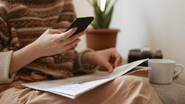 person with newspaper and mobile phone