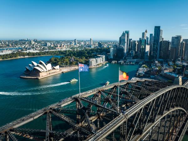 An aerial view of the Sydney shoreline with the iconic Sydney Opera House and Sydney Harbour Bridge crossing the picturesque harbor.