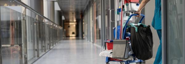 Cleaner pulling cleaning trolley down hallway