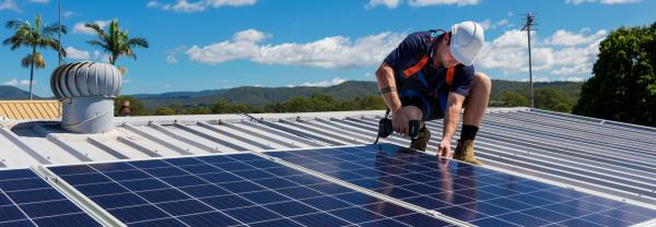 Solar panel technician with drill installing solar panels on household roof