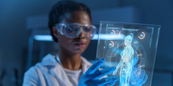 Woman in a white lab coat wearing blue gloves looking at a virtual iPad with a human body on it