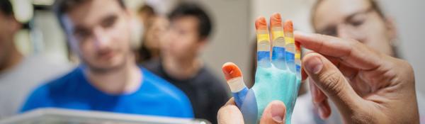 Close up of hands holding a multicolour, multitexture high resolution 3D print as students observe