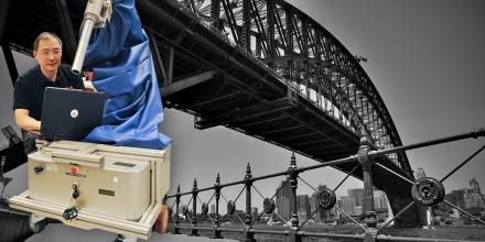 Photo of UTS Professor Dikai Liu and his grit-blasting robot, with the Sydney Harbour Bridge in the background