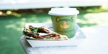 A campus coffee cup sitting in a tray with a sandwich 